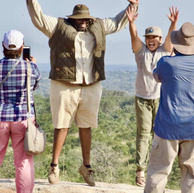 Safari guests celebrating on a rocky lookout overlooking the bush - On Safari Africa